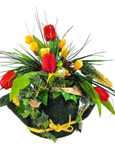 Mit Moos besetzte Gießkanne in der Öffnung ein künstliches Gesteck mit Krokusse und Tulpen aus der Blütenpracht guckt ein witziger Frosch hervor
