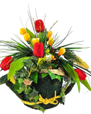 Mit Moos besetzte Gießkanne in der Öffnung ein künstliches Gesteck mit Krokusse und Tulpen aus der Blütenpracht guckt ein witziger Frosch hervor